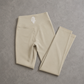 Beige high-waisted leggings folded neatly on a textured gray surface, featuring a small white monogram logo on the waistband.