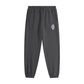 Dark gray tapered jogger pants with a drawstring waist, side pockets, elastic cuffs, and a small white monogram logo on the upper thigh.



