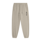 Beige tapered jogger pants with an elastic drawstring waistband, side pockets, elastic cuffs, and vertical black REVIVAL lettering on the upper thigh.

